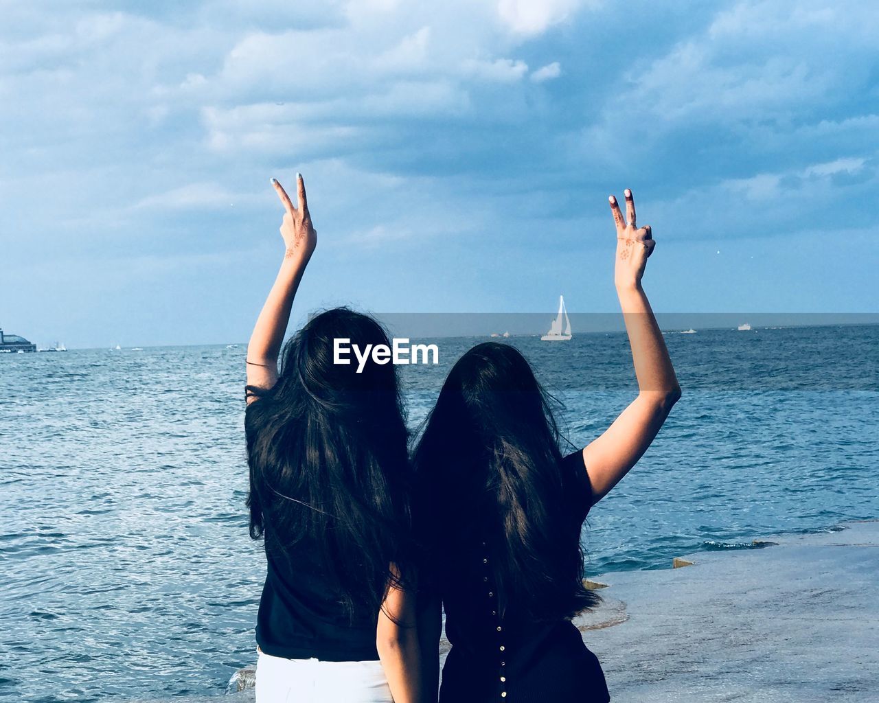 Rear view of female friends gesturing while standing by sea