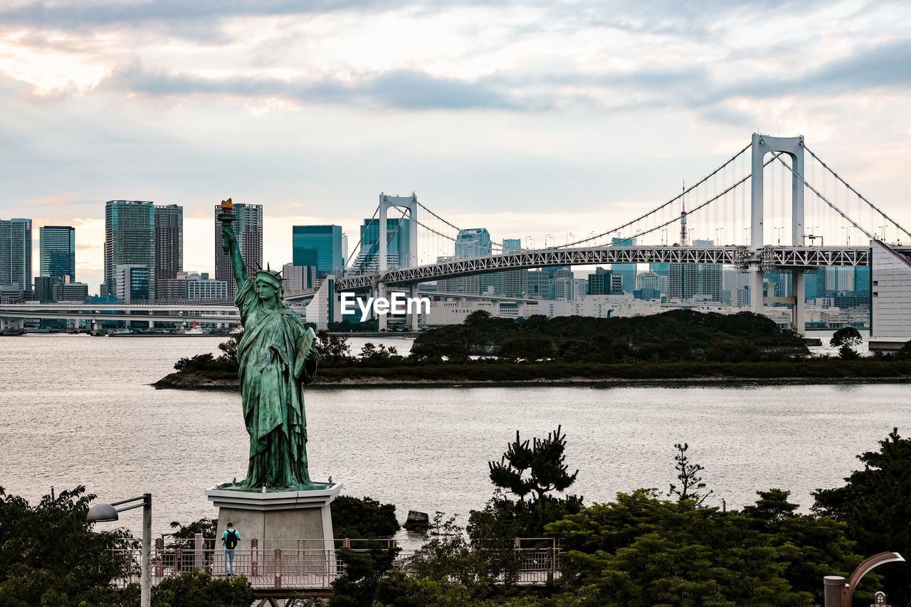 Statue of bridge over city against cloudy sky