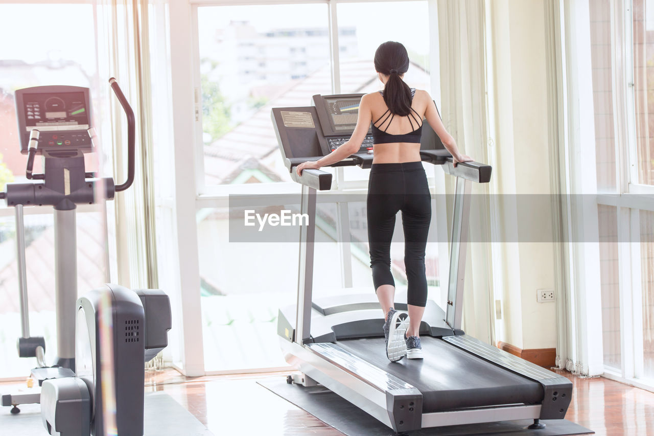 Rear view of woman walking on treadmill in gym