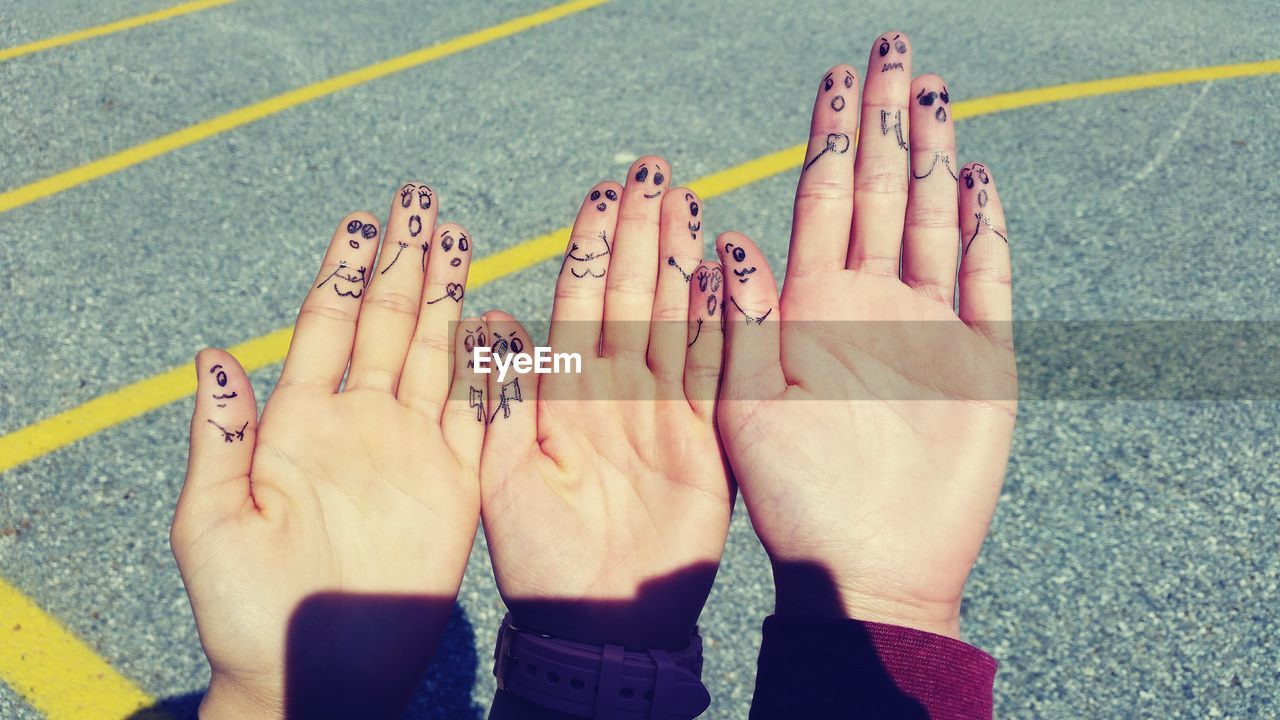 Cropped hands of friends with drawing on fingers against road during sunny day