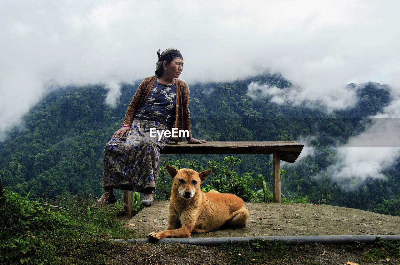 Senior woman sitting on table by dog on mountain