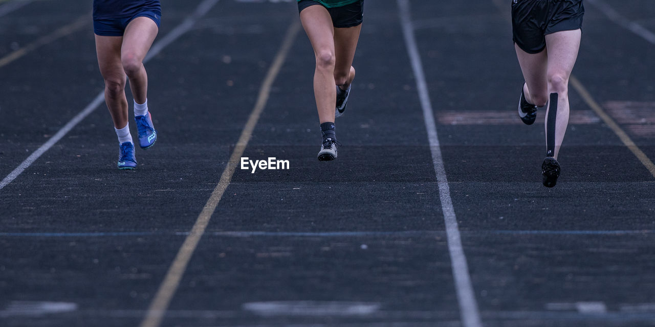 Full frame close-up view of three runners racing side-by-side on a track in lanes to the finish line