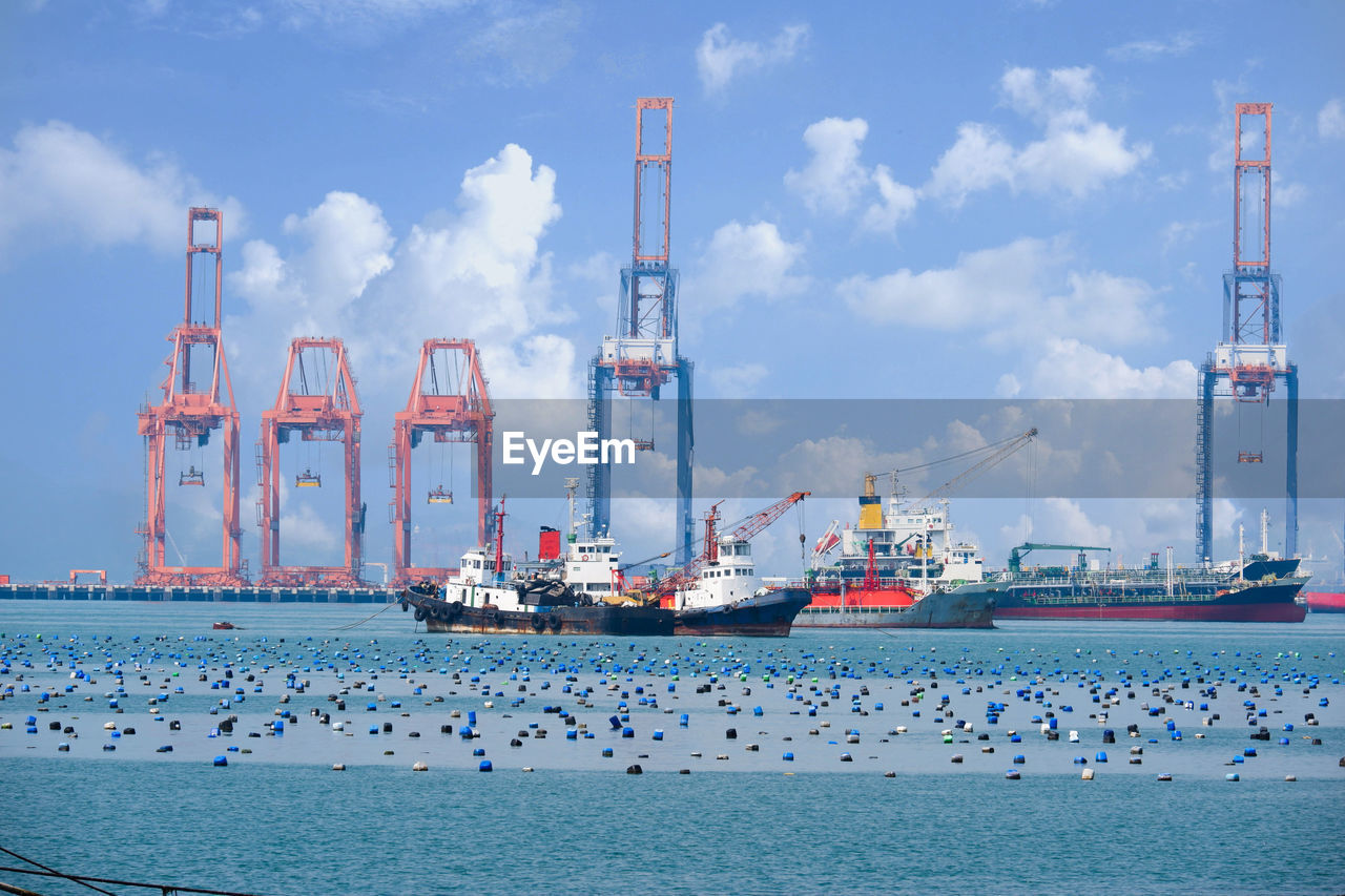 BOATS IN SEA BY COMMERCIAL DOCK AGAINST SKY