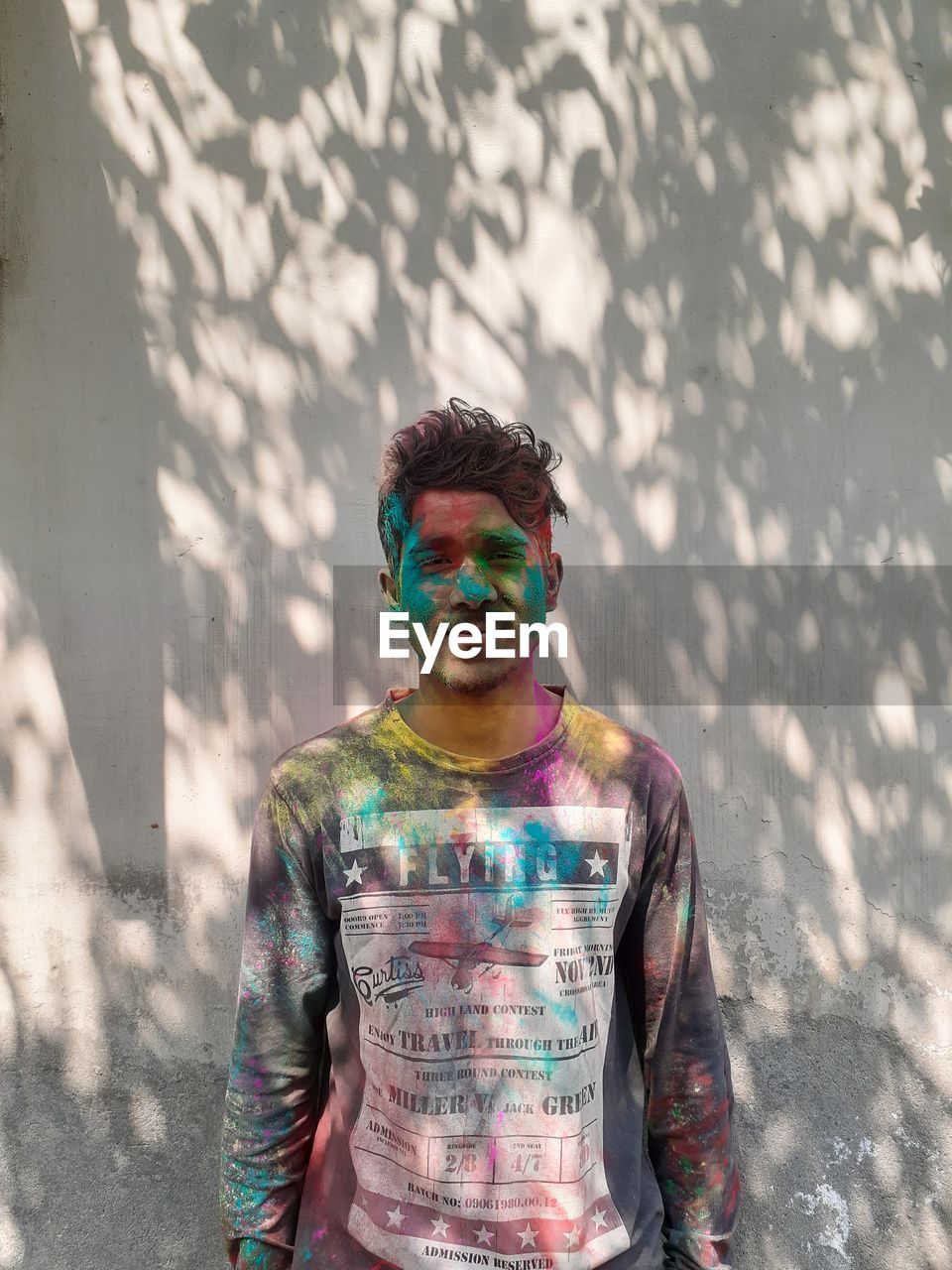 Portrait of young man with powder paint on face standing against wall