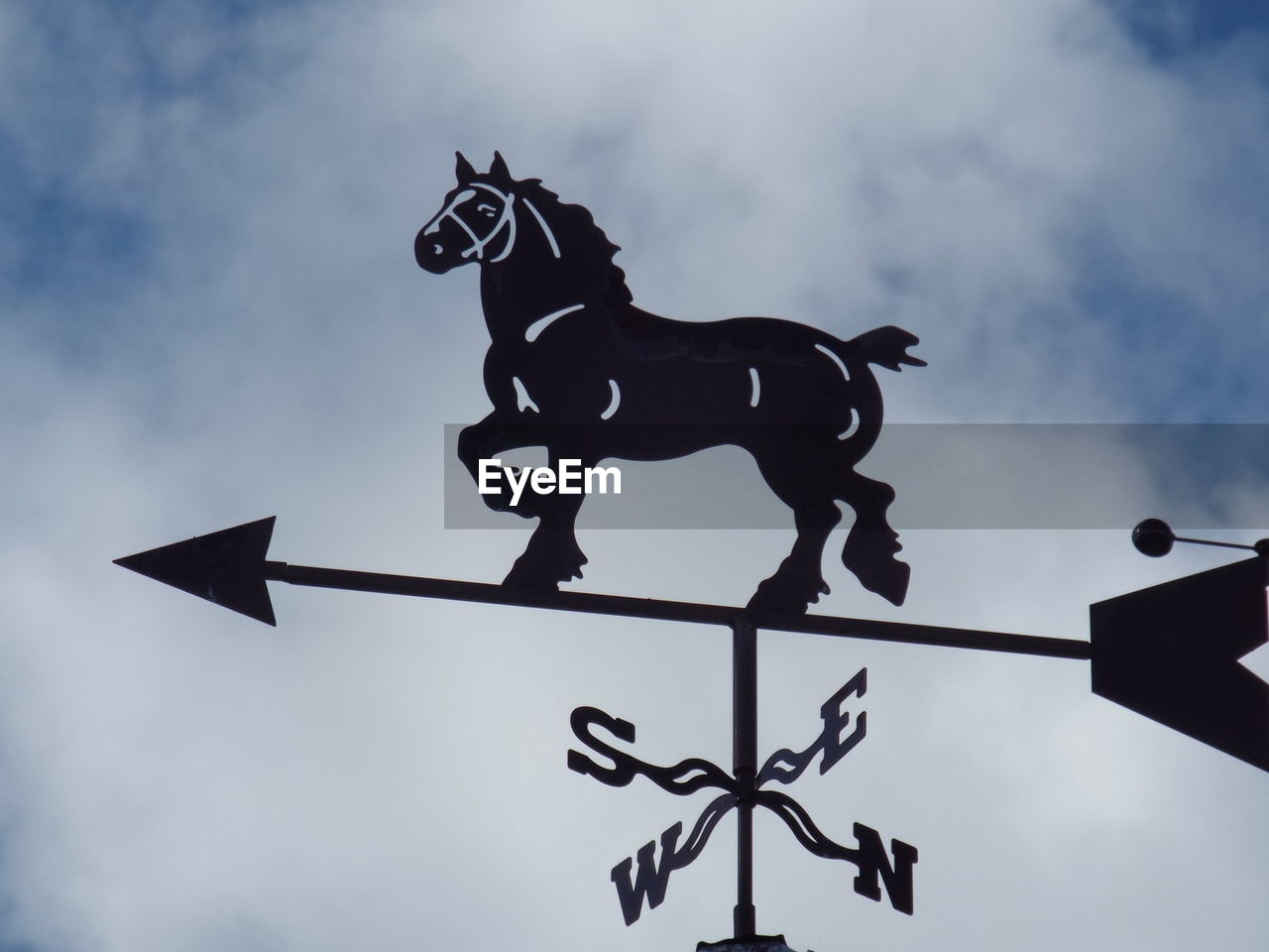 Low angle view of weather vane against cloudy sky