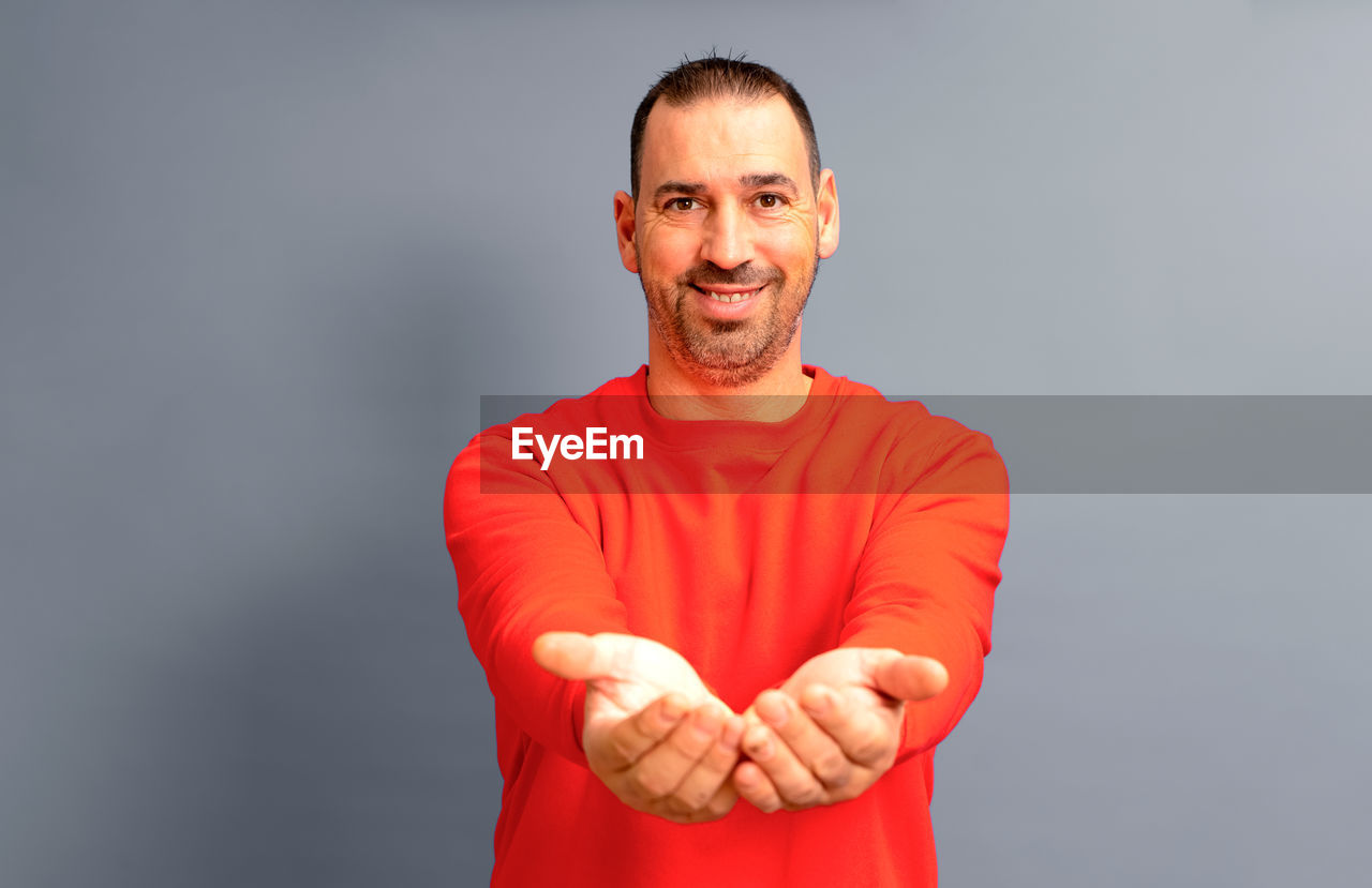 studio shot, adult, one person, portrait, smiling, men, looking at camera, emotion, happiness, indoors, gray background, gray, waist up, person, beard, arms crossed, senior adult, arm, finger, front view, hand, facial hair, clothing, standing, human face, sleeve, casual clothing, positive emotion, cheerful, mature adult, copy space, red, human mouth, teeth, smile, t-shirt, lifestyles