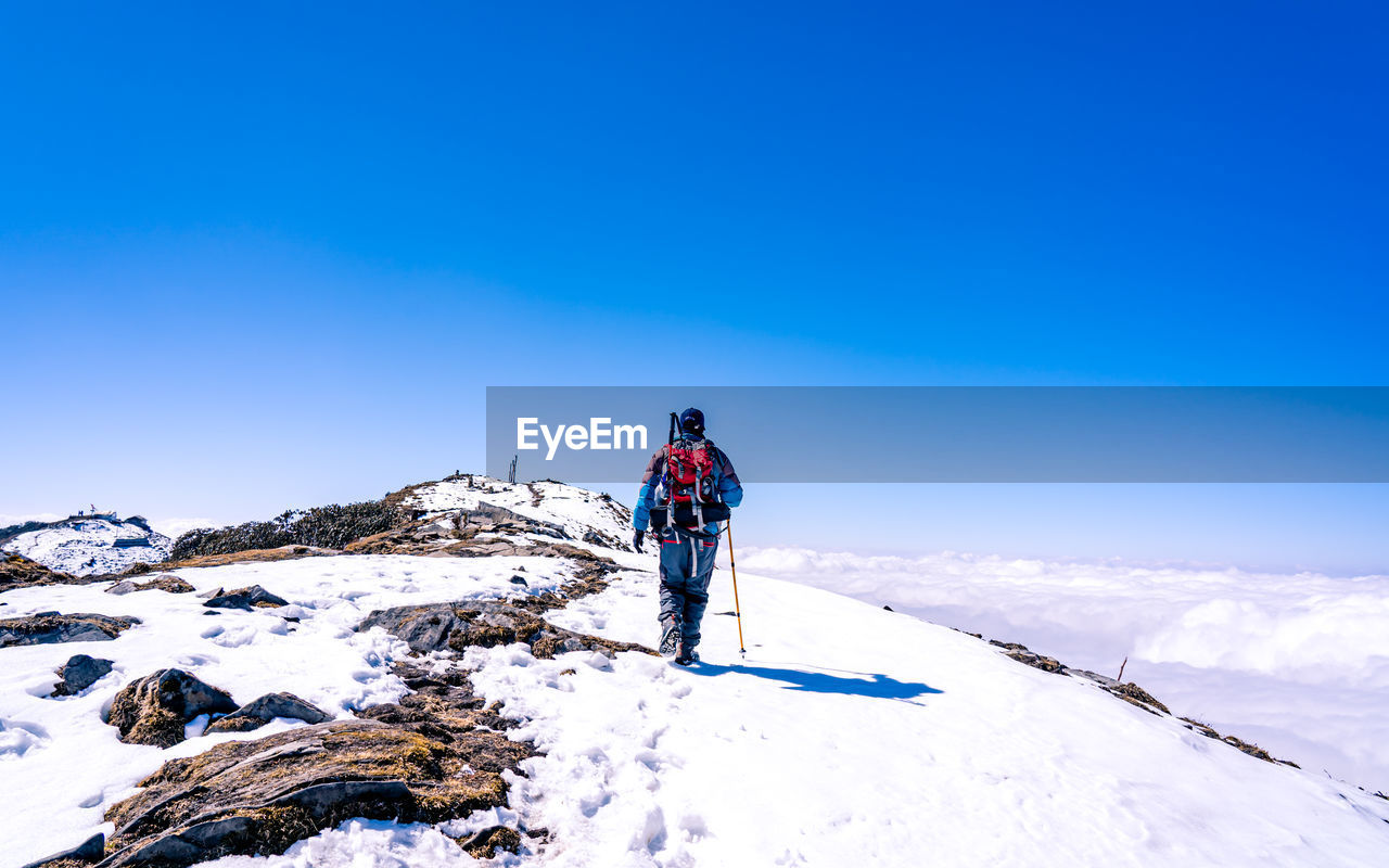 WOMAN ON SNOW COVERED MOUNTAIN AGAINST BLUE SKY