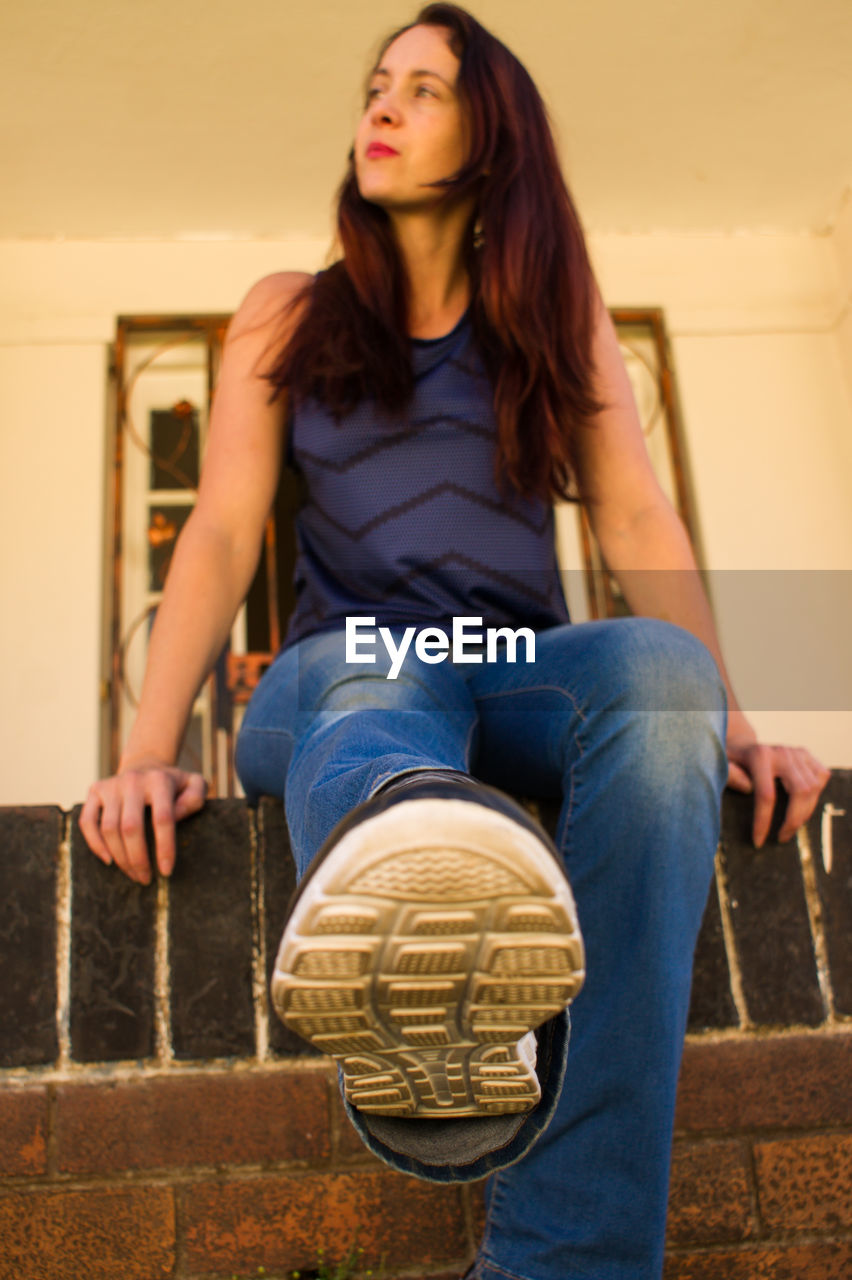 BEAUTIFUL WOMAN SITTING AGAINST WALL