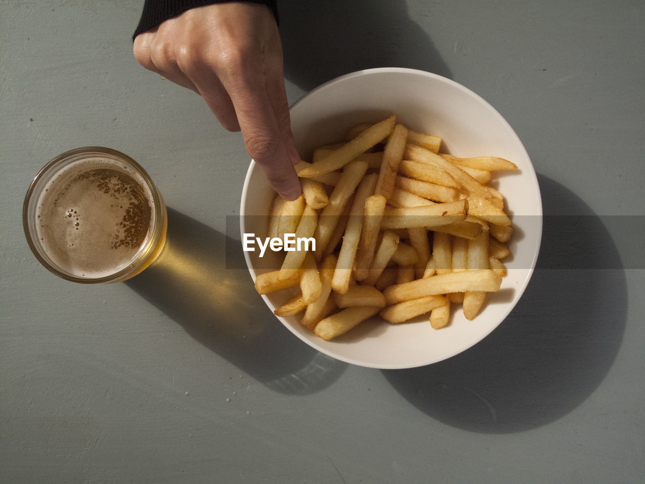 Cropped hand reaching towards french fries by beer on table