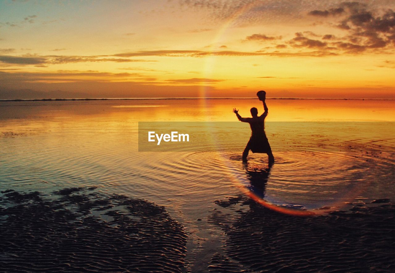 Silhouette man with arms raised while standing in sea against sky