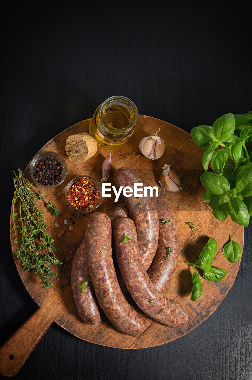 food and drink, food, freshness, herb, studio shot, healthy eating, vegetable, wood, sausage, meat, spice, no people, kielbasa, wellbeing, black background, rustic, ingredient, indoors, plant, high angle view, cutting board, meal, still life, fast food, boudin, dark, household equipment, leaf, fruit, directly above, italian sausage