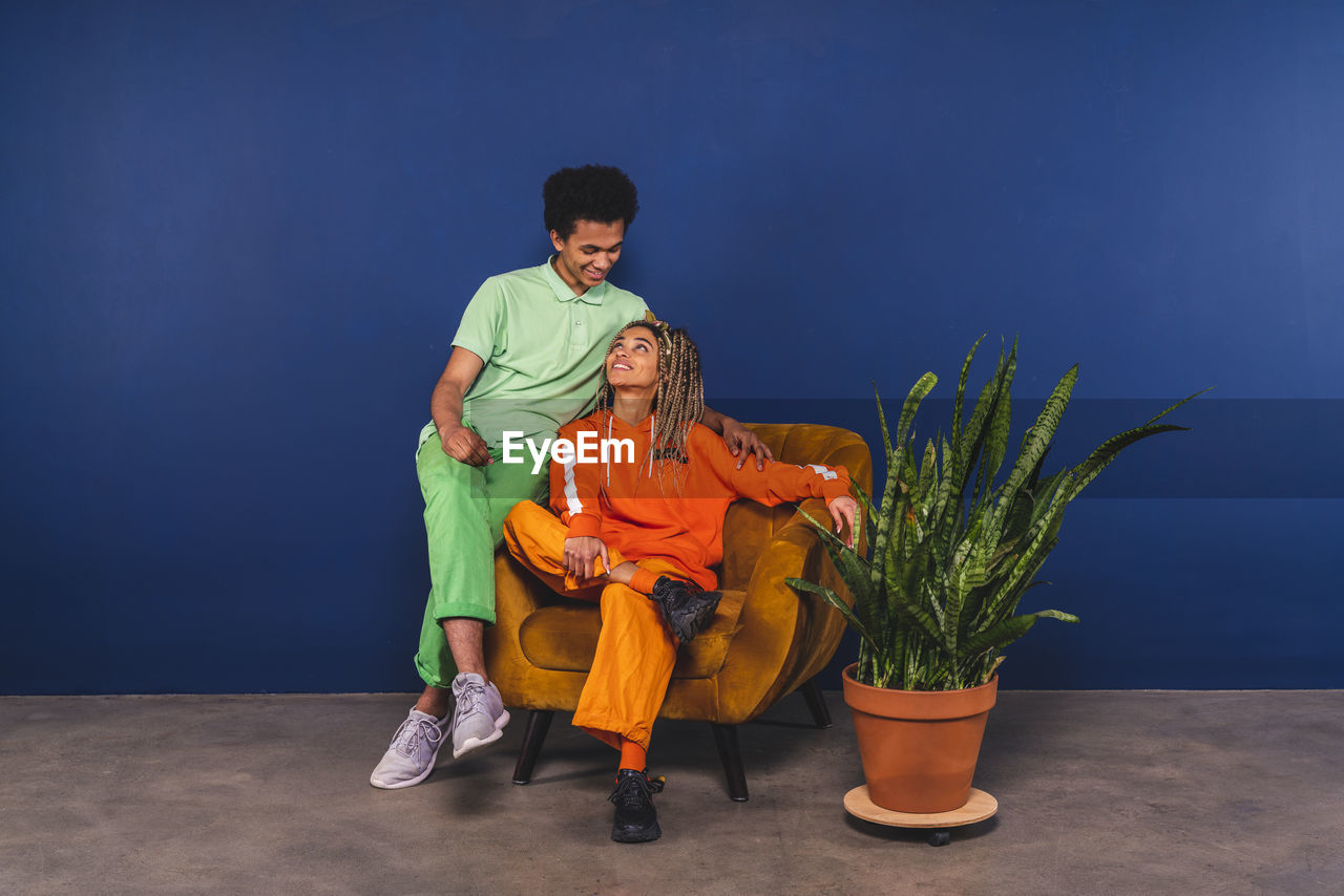 Friends looking at each other while sitting on armchair at studio