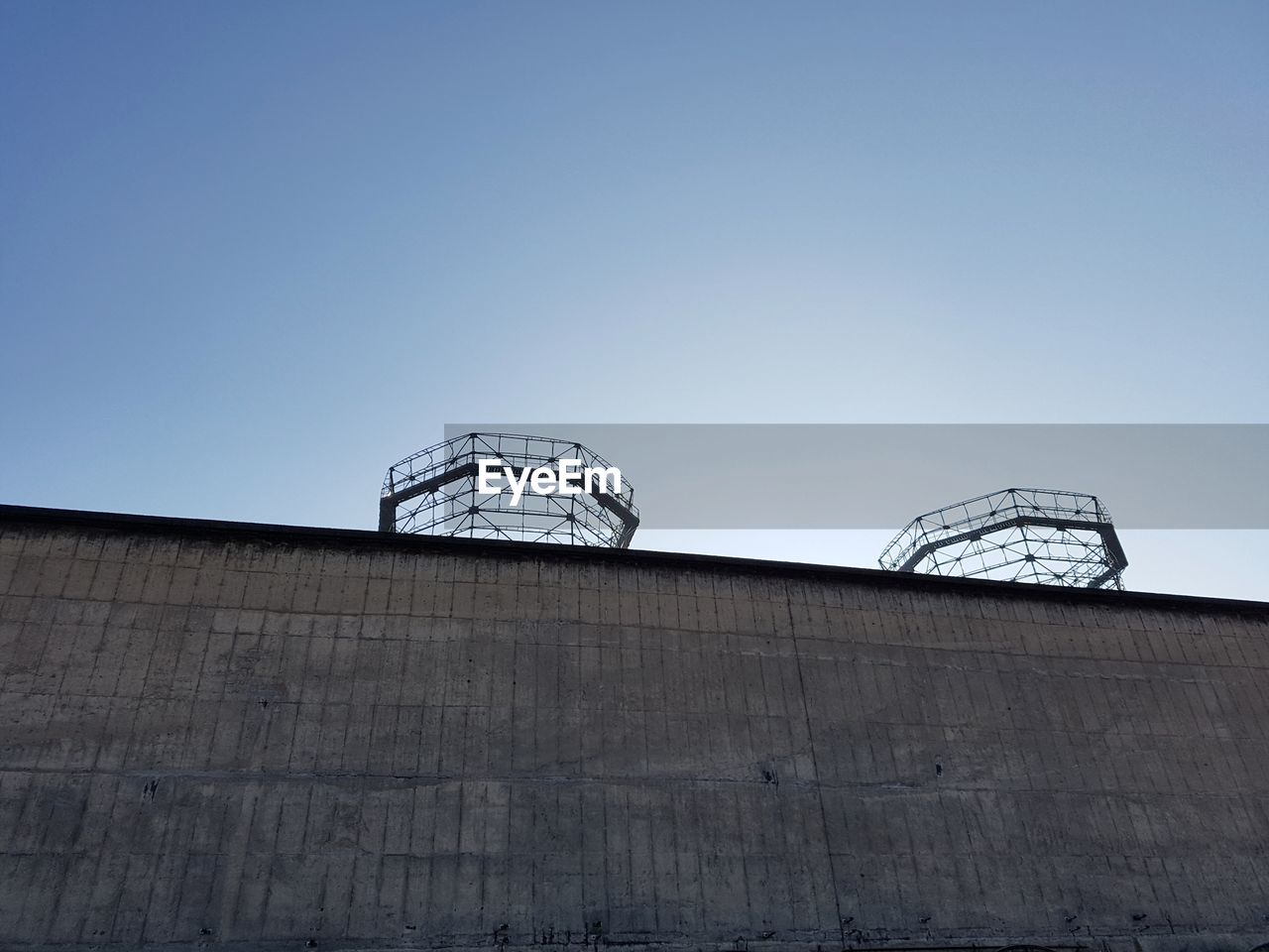 Low angle view of metallic structures by wall against clear sky