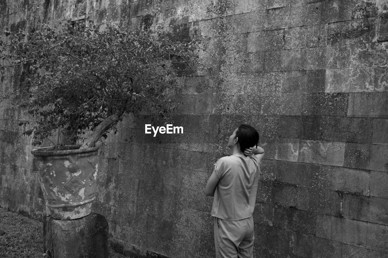 Rear view of woman looking at plant while standing by wall