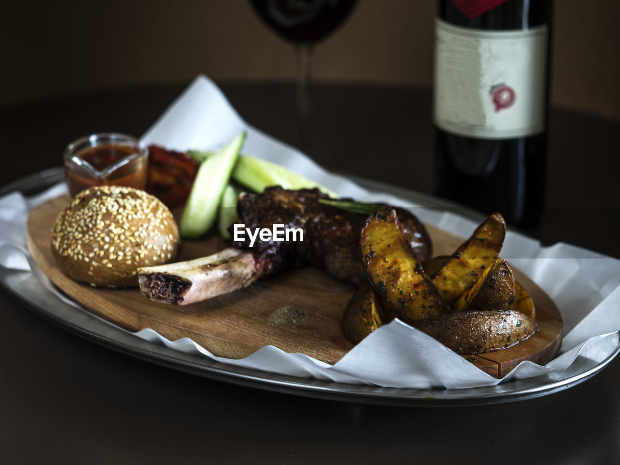 Grilled steak on bone veal with baked potatoes and bun served in tray on table