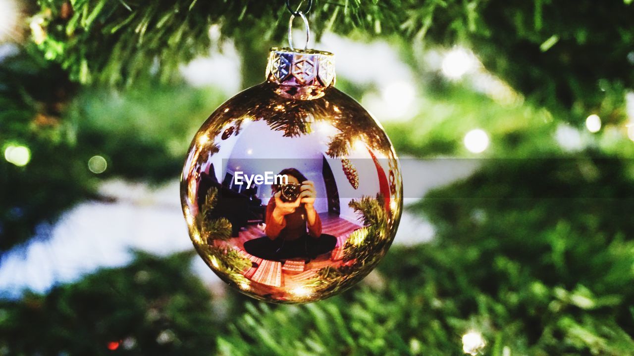 Reflection of woman in bauble hanging on christmas tree