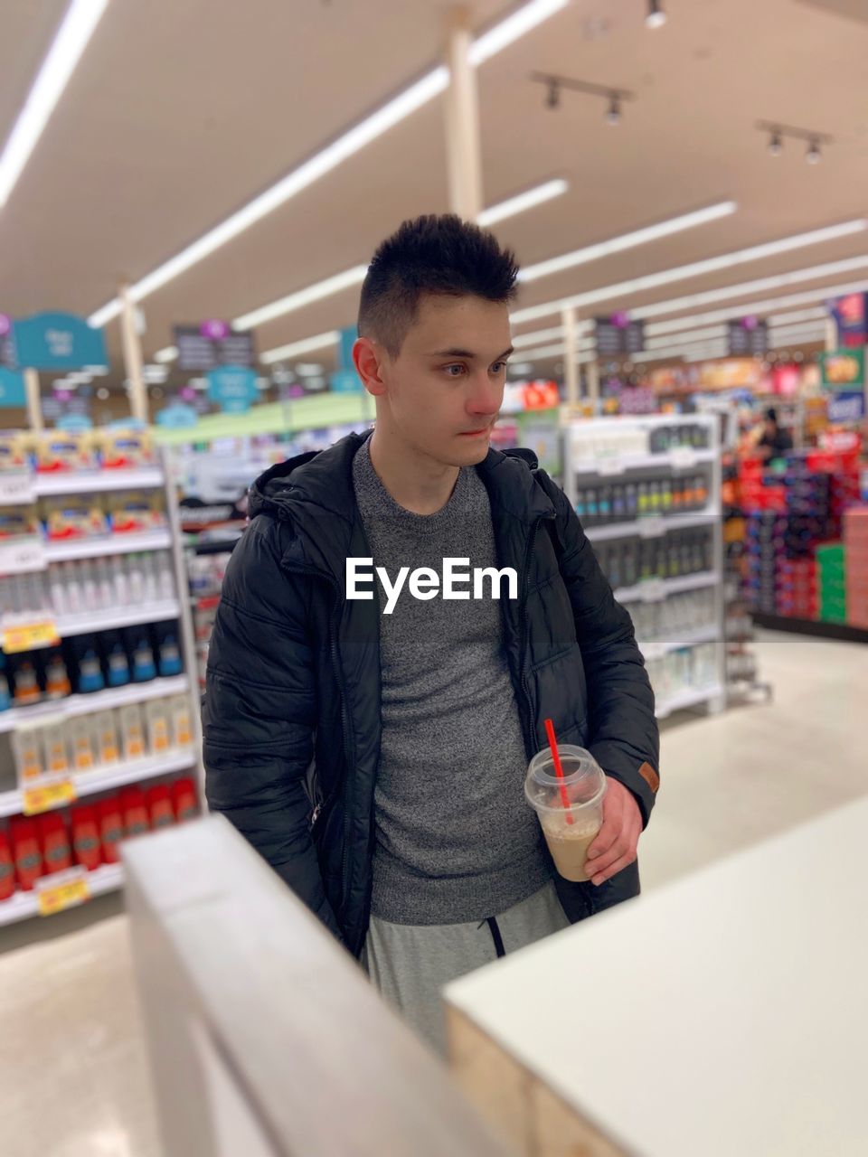 Young man holding coffee cup standing in shopping mall