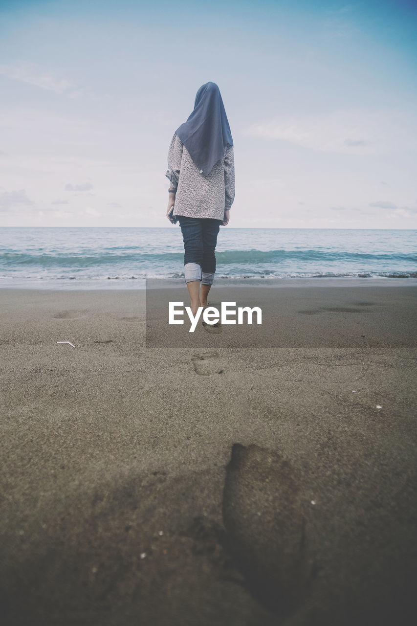 Rear view of woman on beach against sky