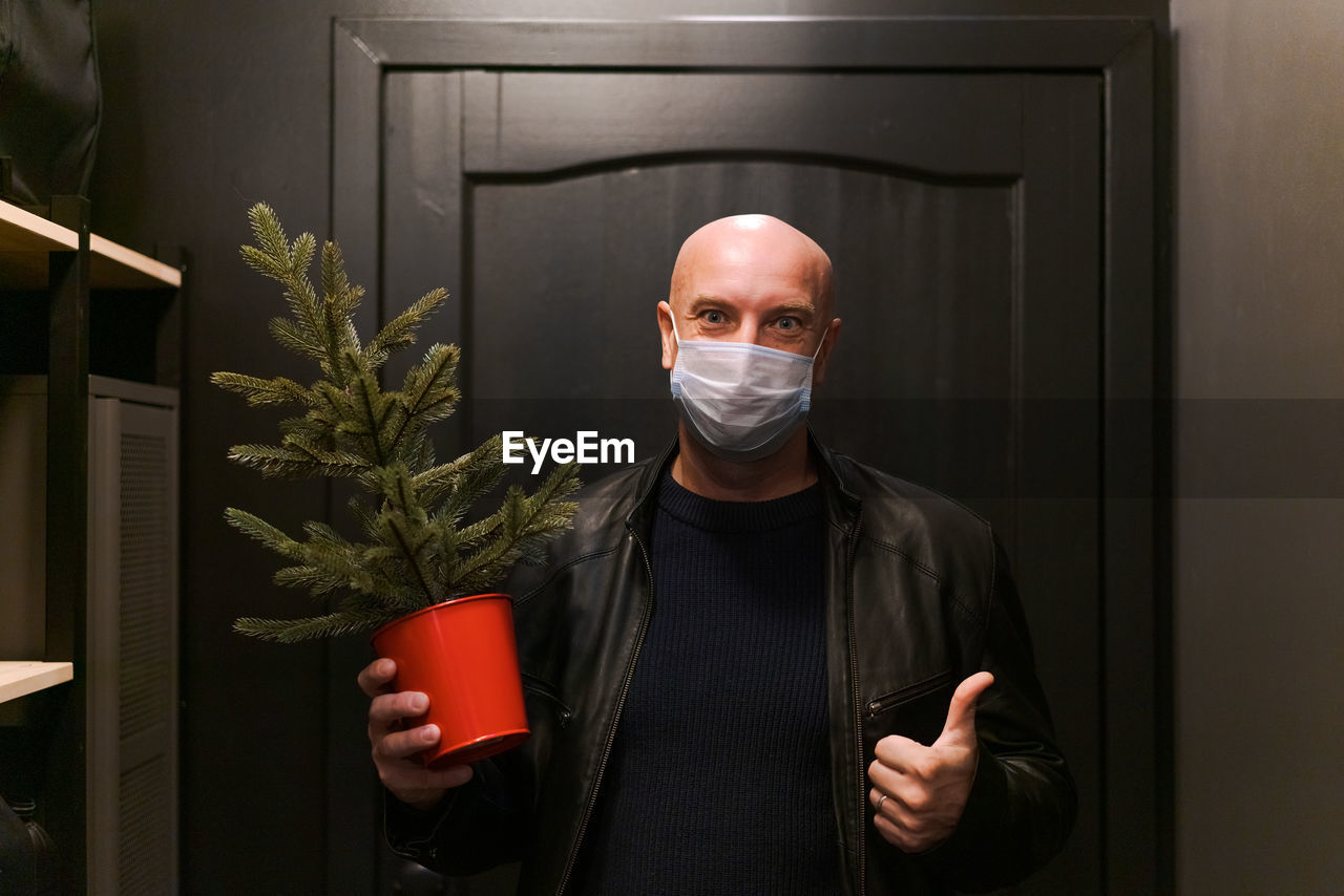 A bald man in protective mask stands in doorway with small artificial christmas