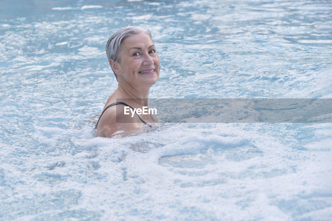 Senior caucasian woman with gray short wet hair enjoying in outdoor thermal swimming pool.