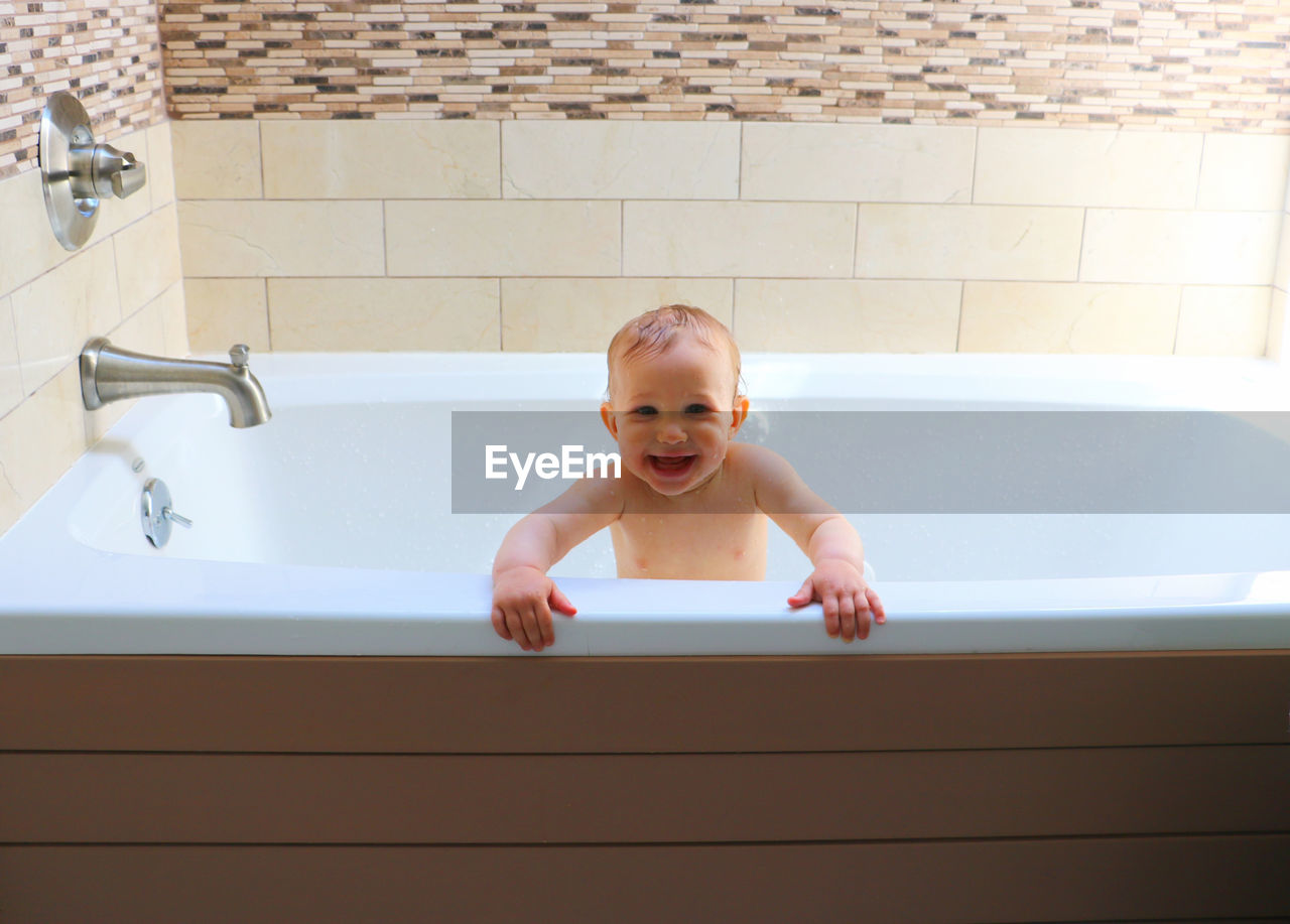 High angle view of cute smiling baby taking a bath, standing in a bathtub