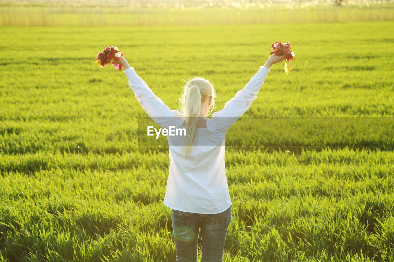 Rear view of woman standing in field with flowers