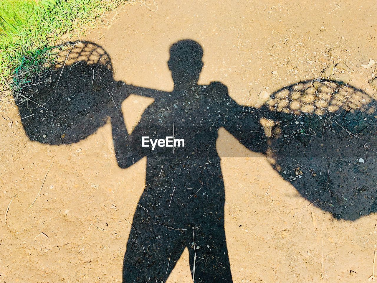 Shadow of man carrying containers on land