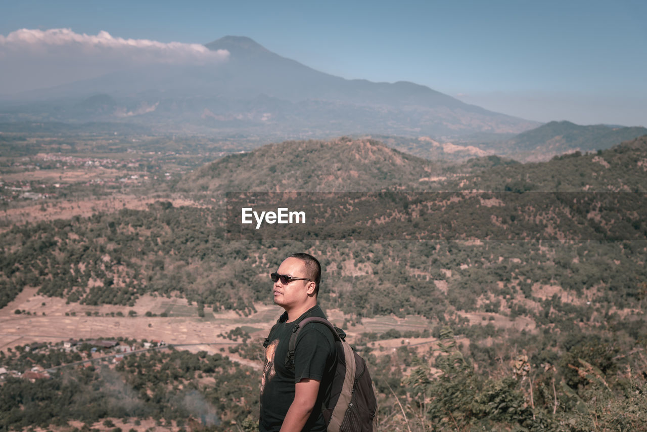 Portrait of young man standing on landscape against sky