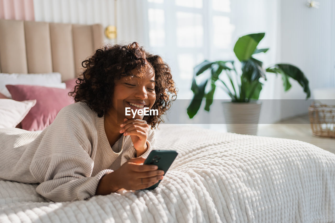 young woman using mobile phone while lying on bed at home