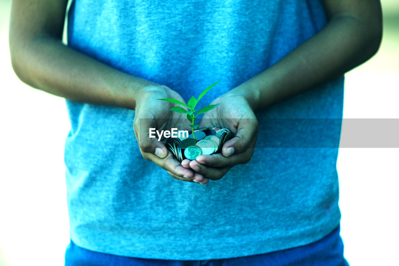 Midsection of man holding seedling and coin