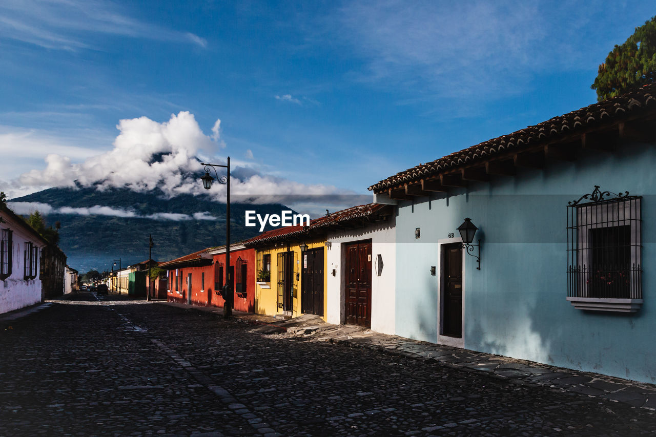 Diminishing perspective of road amidst houses against blue sky