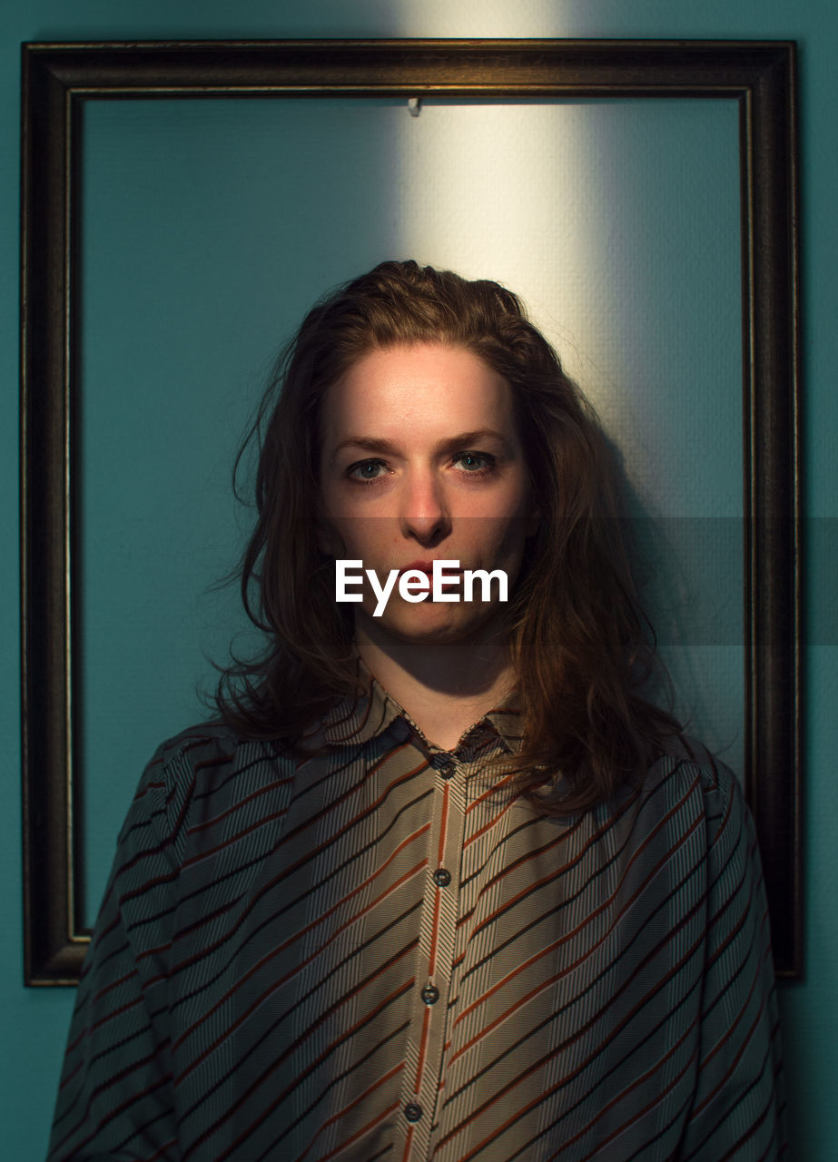 Mid adult woman standing against picture frame on wall