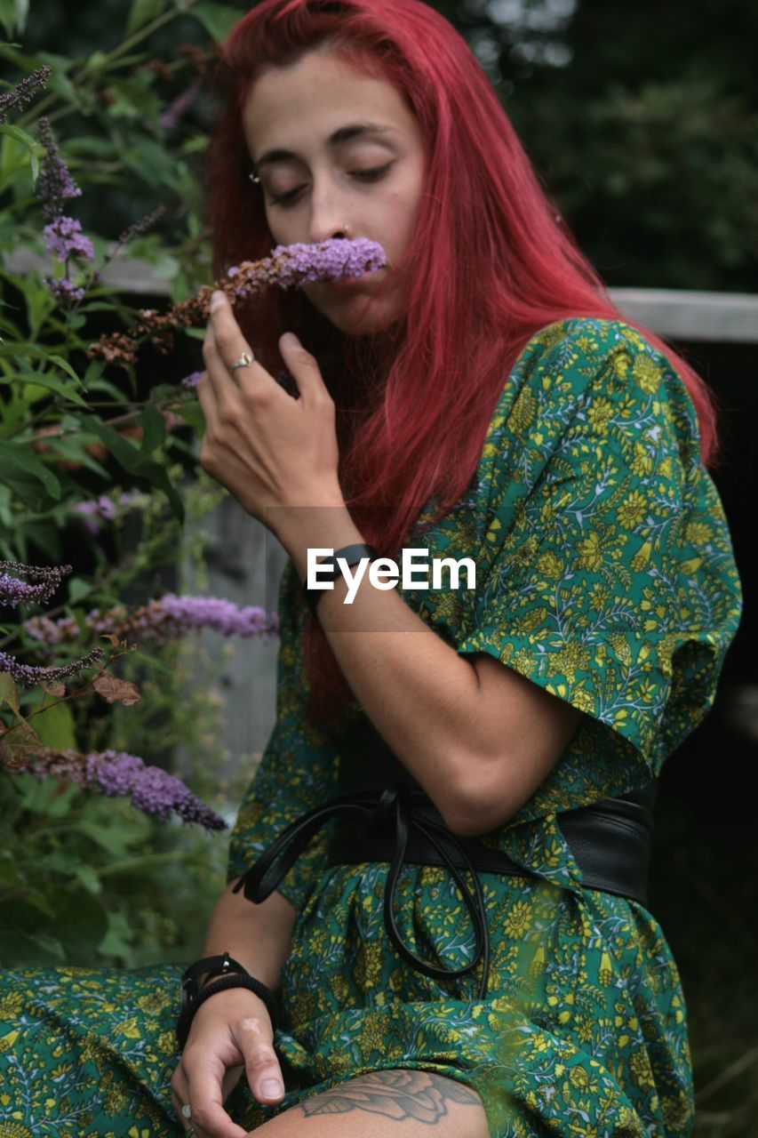 Young woman with red hair and a long green dress, smelling a lilly flower 