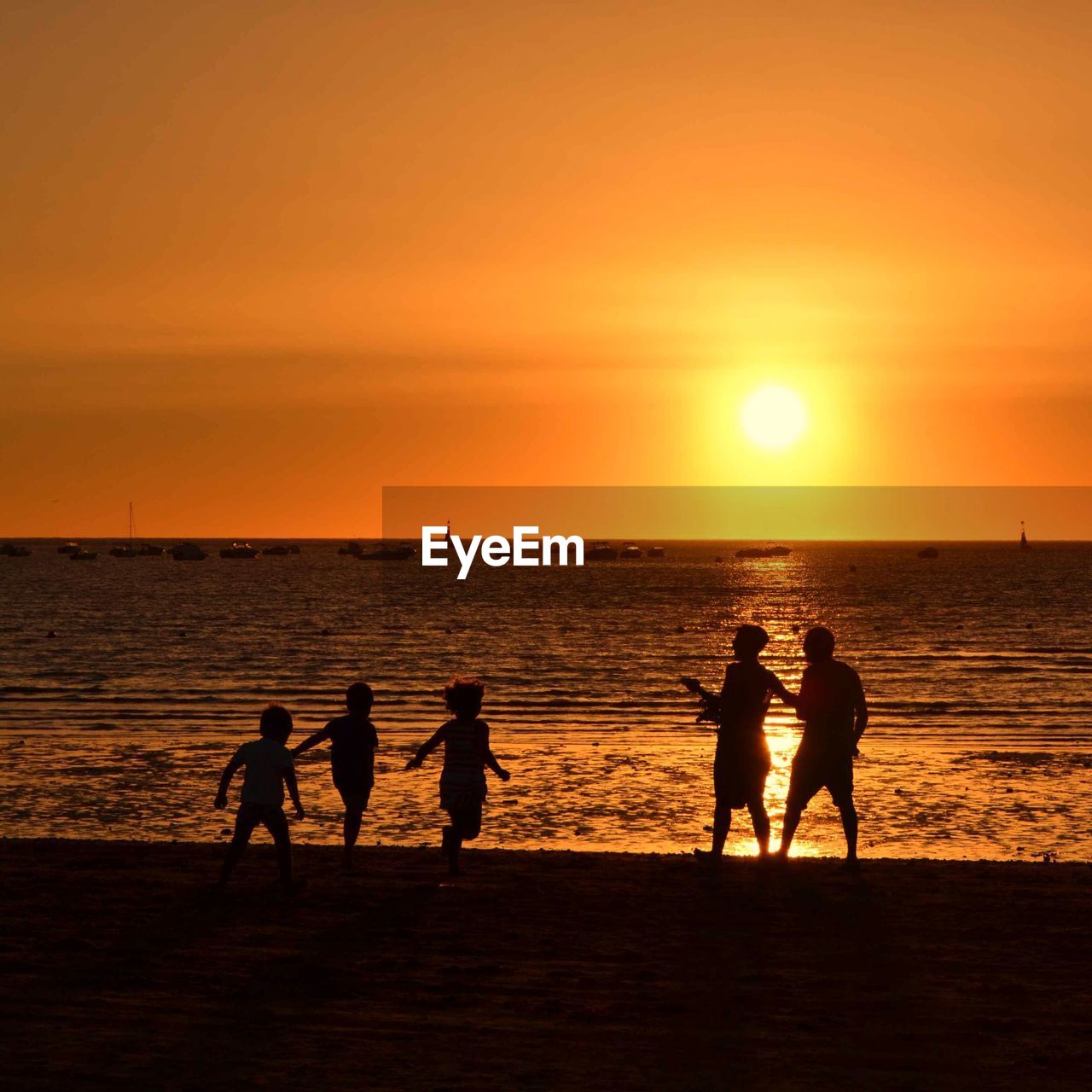 Silhouette of people at beach against orange sky