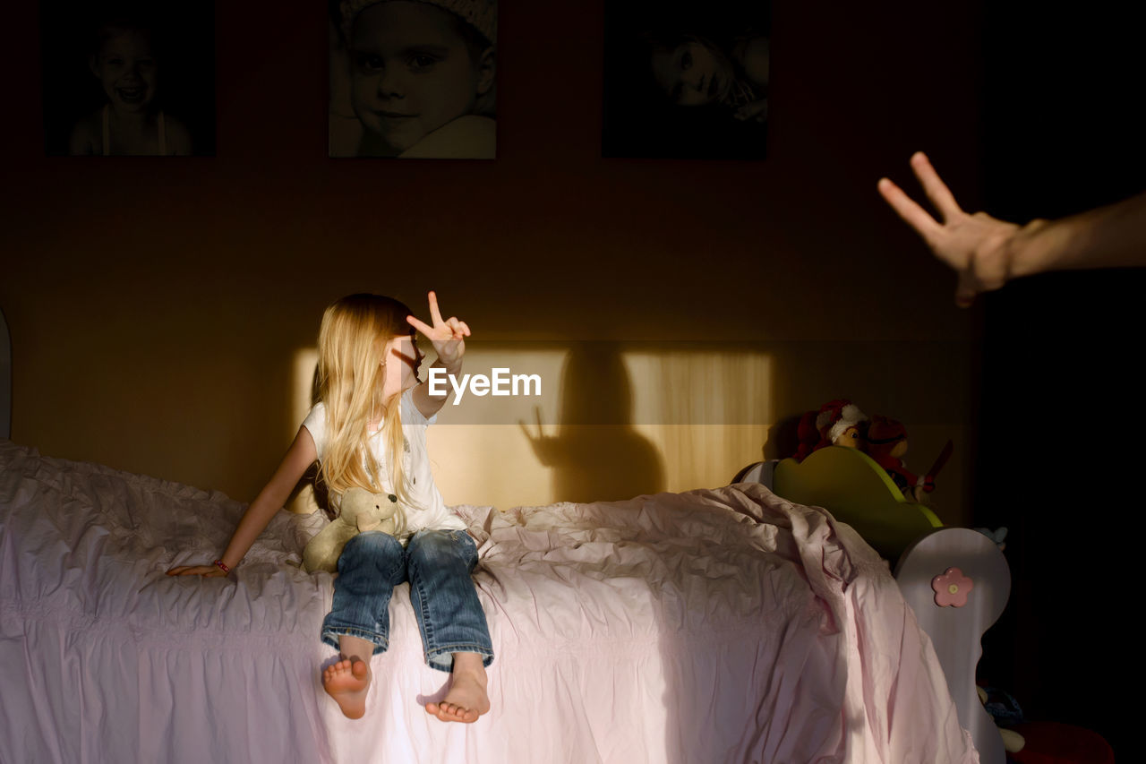 Happy girl showing peace sign while sitting on bed at home