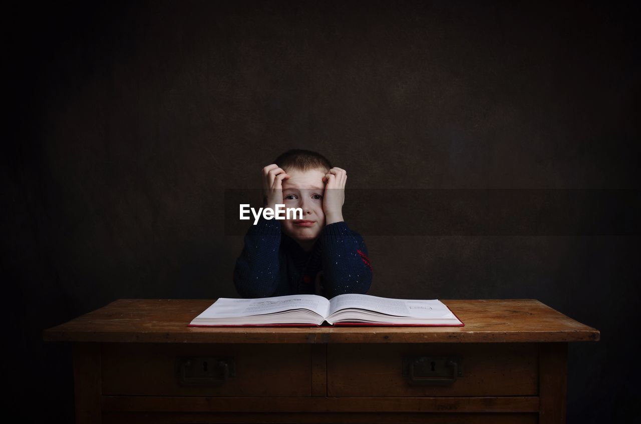 Portrait of stressed boy with book on table 