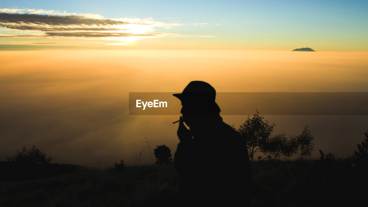 Silhouette man smoking against sky during sunset