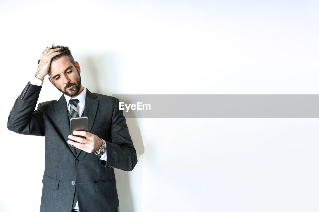 MID ADULT MAN USING SMART PHONE WHILE STANDING ON WALL