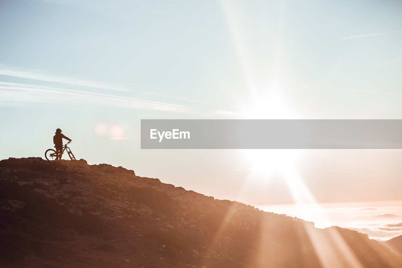 Side view of guy in helmet riding on bicycle on top of mountain with beautiful sunset