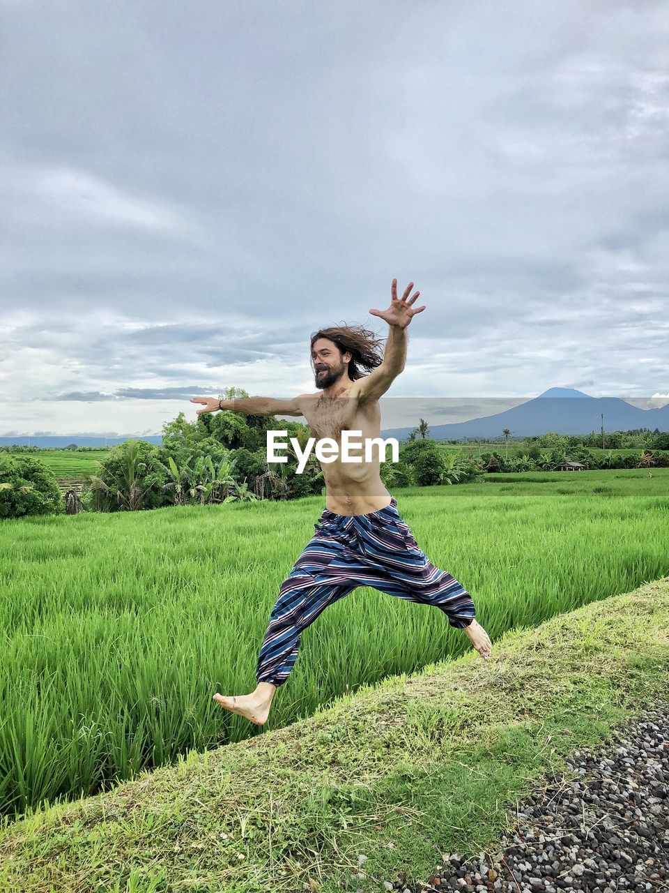 WOMAN JUMPING ON FIELD AGAINST SKY