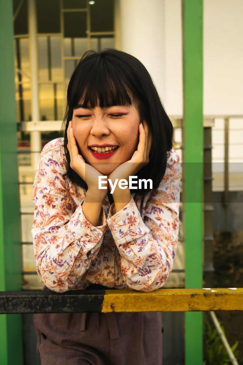 PORTRAIT OF A SMILING YOUNG WOMAN STANDING OUTDOORS