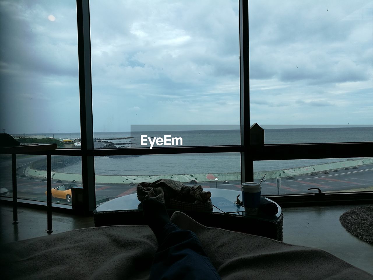 LOW SECTION OF PERSON BY SEA AGAINST SKY SEEN THROUGH WINDOW