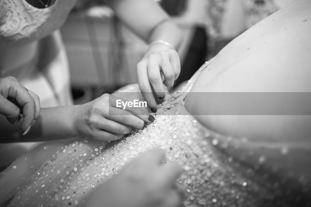 Cropped hands of bridesmaid adjusting wedding dress of bride