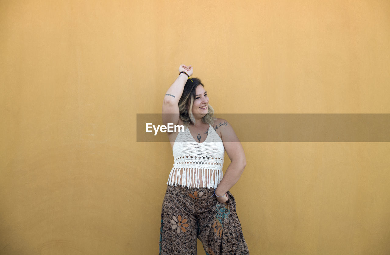 Portrait of smiling young woman dancing against yellow wall in summer