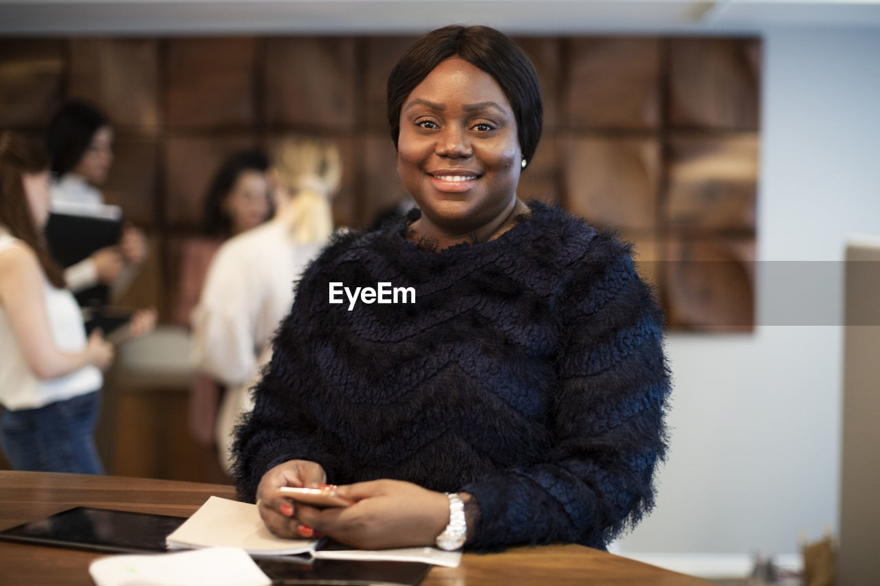 Portrait of smiling female entrepreneur with smart phone at desk