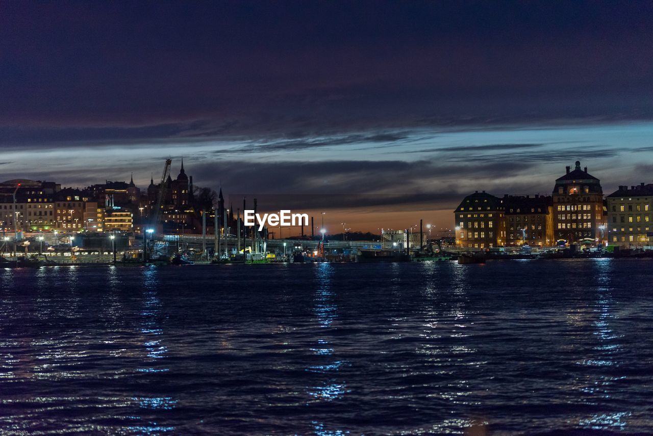 Illuminated buildings at waterfront during sunset