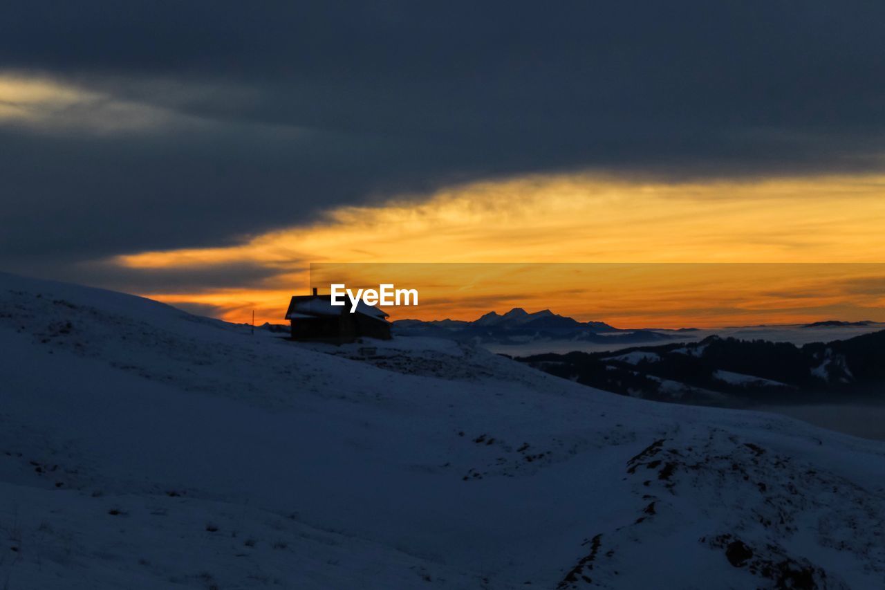 Snow covered landscape against sky during sunset