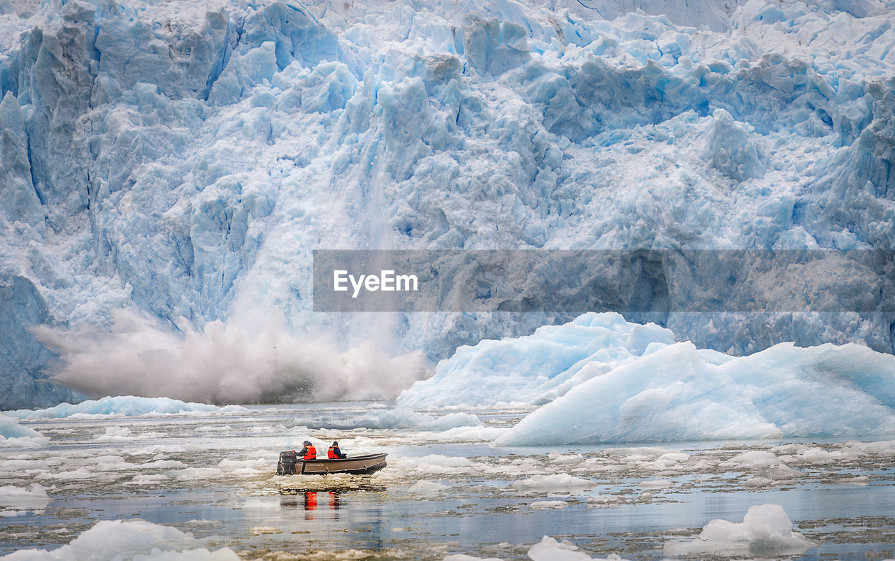 People in boat on frozen lake against glacier
