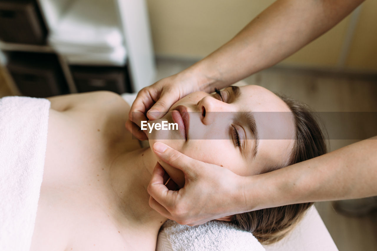 Masseur doing massage on a woman's face at the spa.