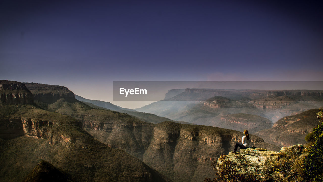 Woman sitting on mountains against clear sky